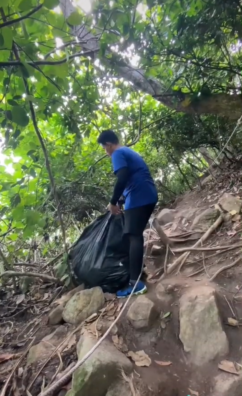 Hiker carries a huge garbage bag of trash.