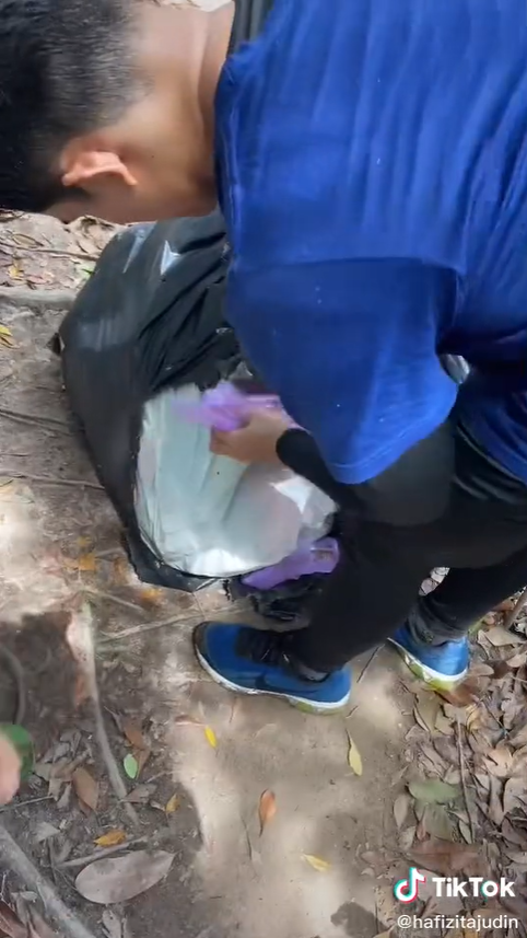 Hiker picks up more trash and places it into his bag.
