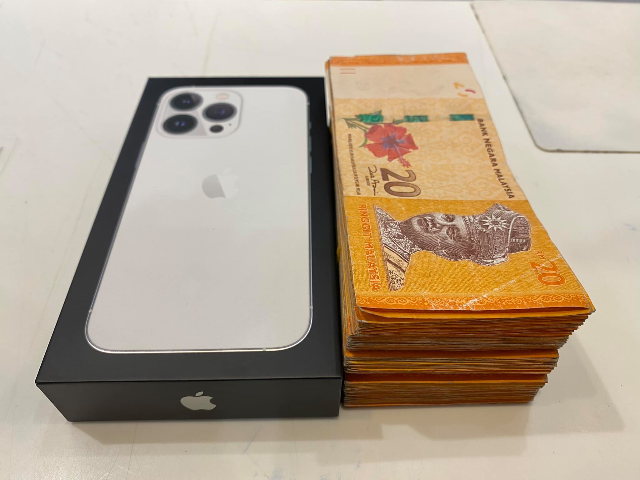 An iPhone 13 Pro next to a stack of RM20 notes.