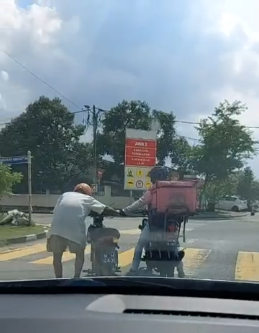 A food delivery rider helping out an elderly man, approaching a road shoulder.