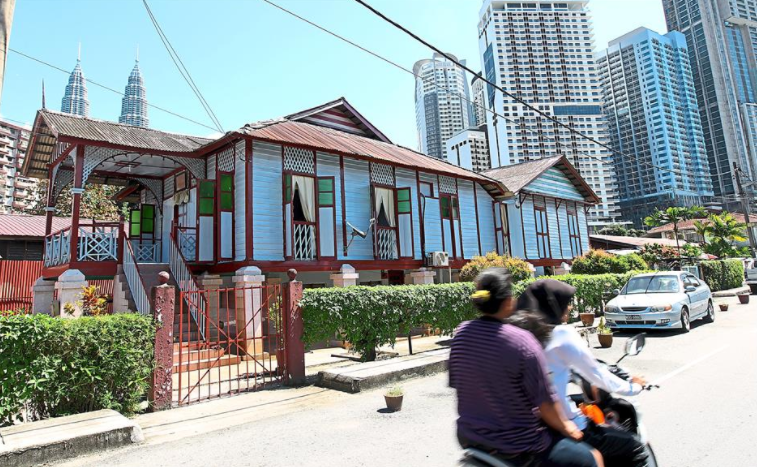 Motorcyclists riding past a house in Kampung Baru. 