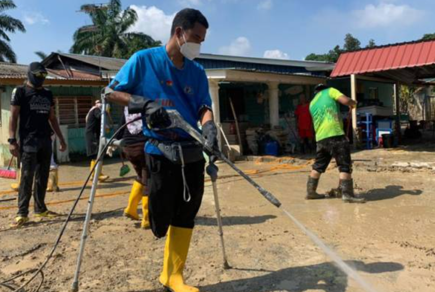 Mr Shukor using crutches to get around, helping flood victims clean their homes.