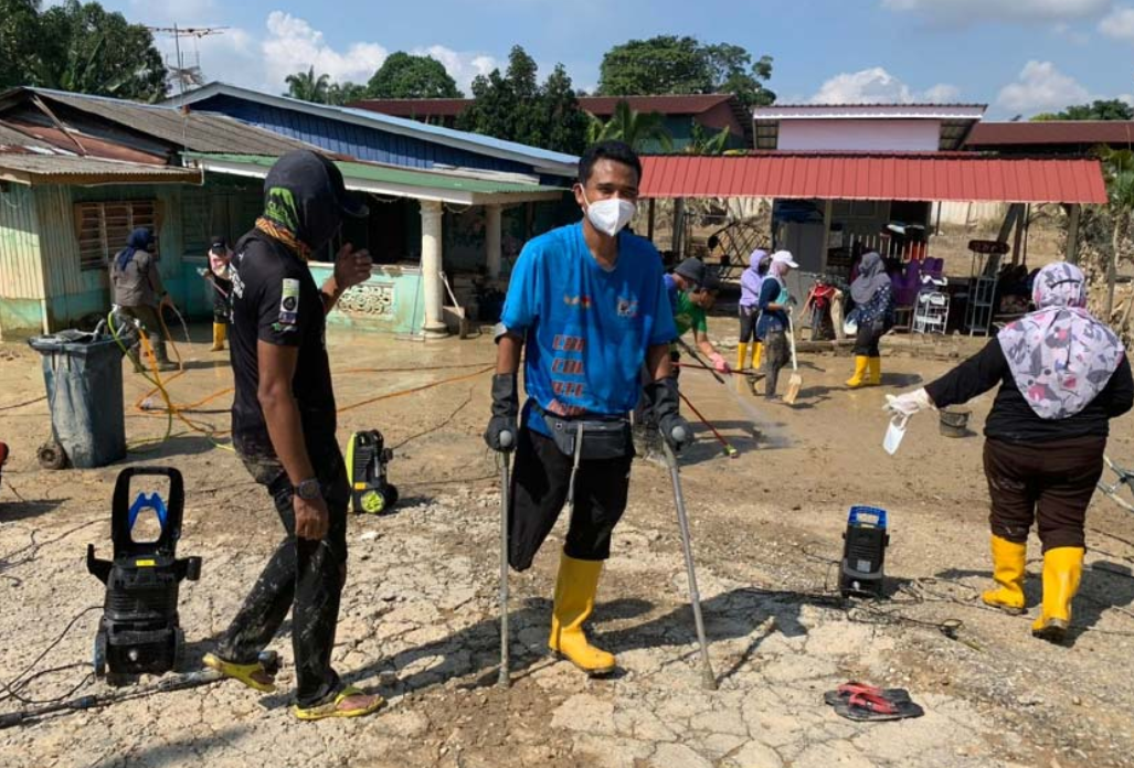 Mr Shukor using crutches to get around, helping flood victims clean their homes.