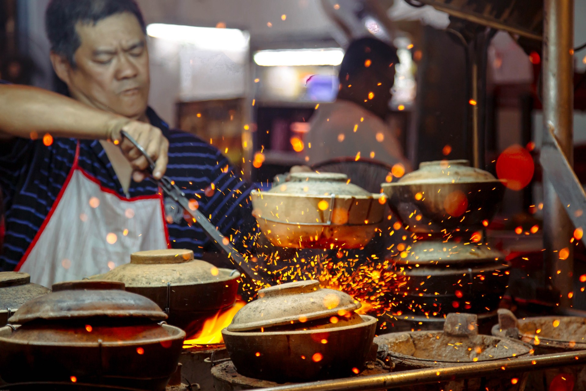 A cook tending to claypots filled with chicken rice at a local hawker stall. 
