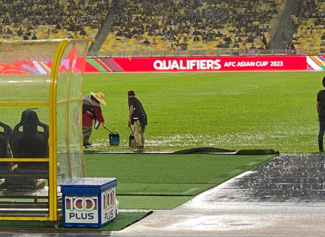 Bukit Jalil stadium employees were seen using dustpans to try and drain the field of excess rainwater. Image credit: Malaysia Gazette